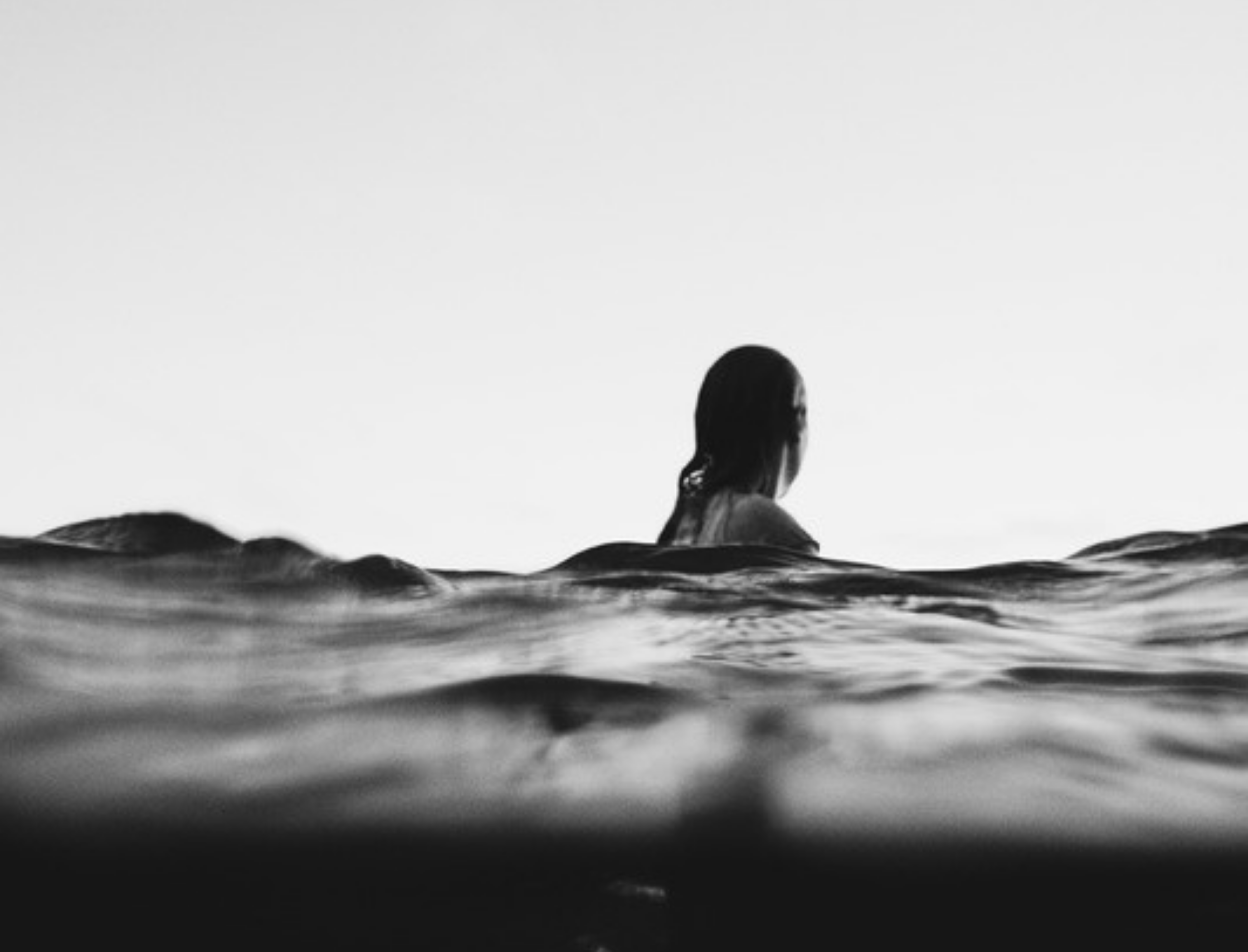 sea surface at eye level, dark choppy water with a girl standing in the water with her back to us in the background