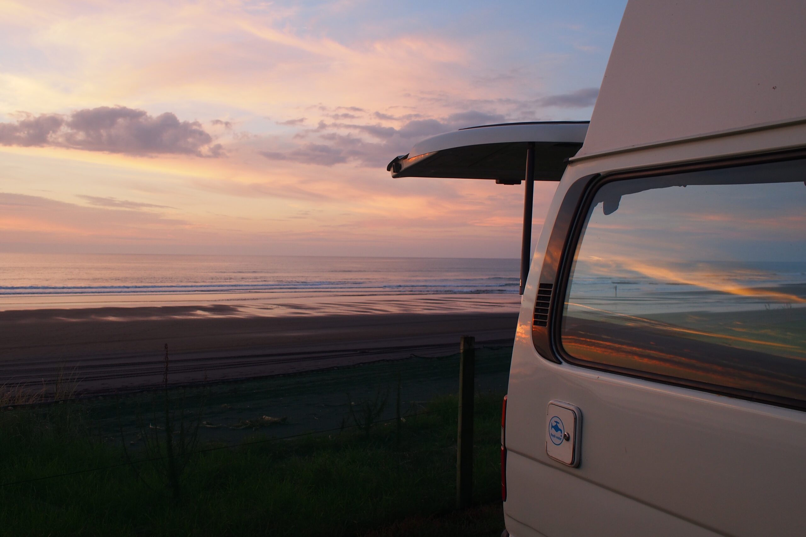 Sunset at the beach with the back of a campervan in the right foreground, back door open